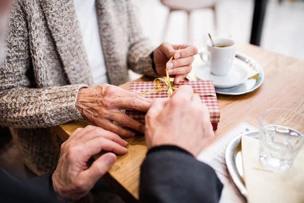 Casal sénior com um presente num café. Tempo de Natal . — Fotografia de Stock