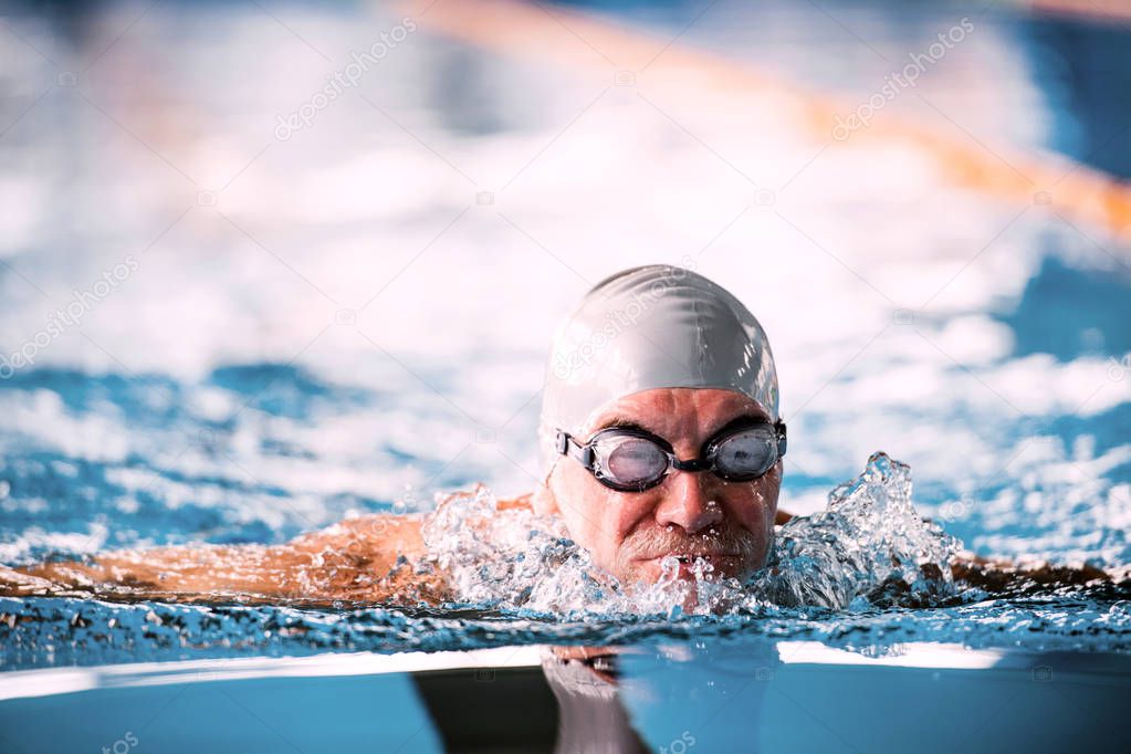 Senior man swimming in an indoor swimming pool.