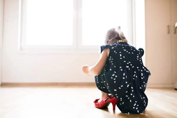 Αγνώριστος μικρό κορίτσι στο φόρεμα και κόκκινο ψηλά τακούνια στο σπίτι. — Φωτογραφία Αρχείου