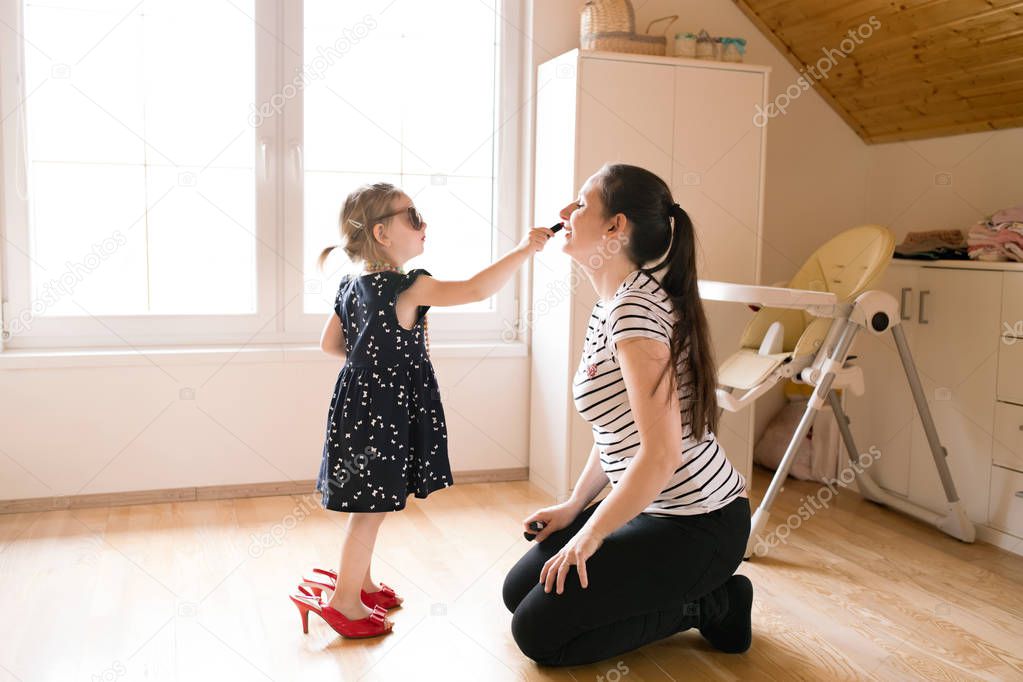 Little girl doing make-up to her attractive mother with lipstick