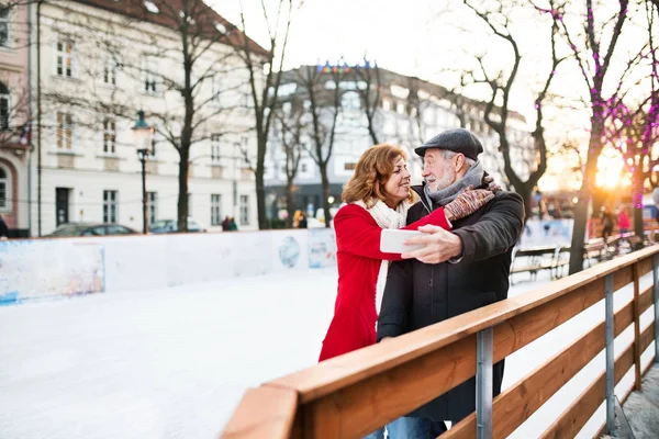 Senior paar met smartphone op een wandeling in een plaats (city) in de winter. — Stockfoto