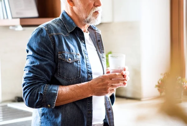 Uomo anziano che tiene un bicchiere d'acqua in cucina . — Foto Stock