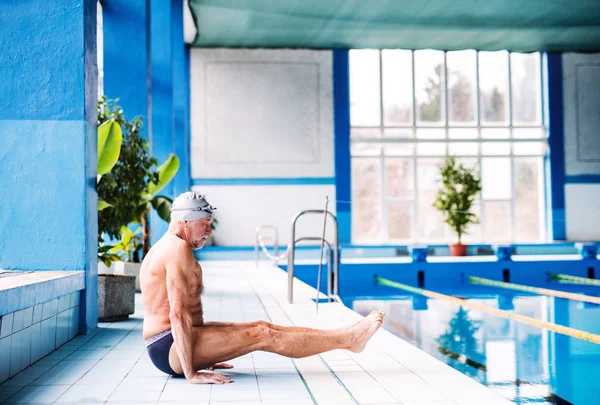 Senior man die zich uitstrekt van het overdekte zwembad. — Stockfoto
