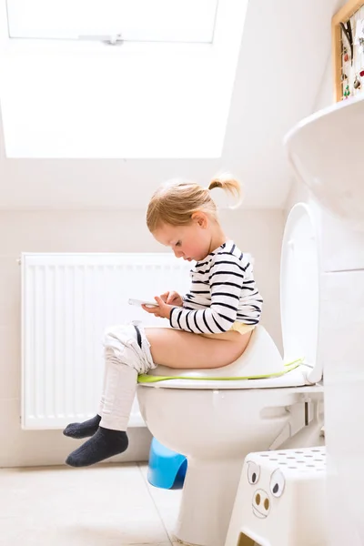 Fetiță cu smartphone stând pe toaletă . — Fotografie, imagine de stoc