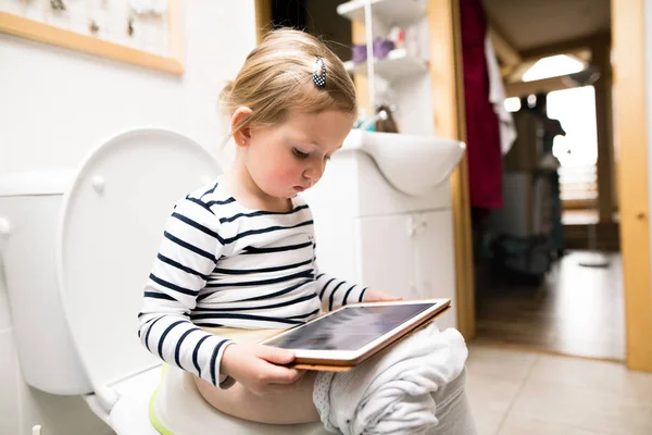 Niña con la tableta sentada en el inodoro . — Foto de Stock