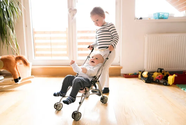 Oyuncak bebek arabası bebek kardeşi ile küçük kız evde. — Stok fotoğraf