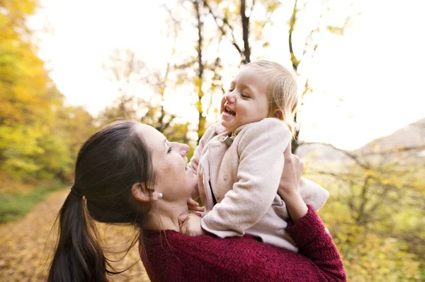 Anne ve kızı sonbahar ormandaki bir yolda.