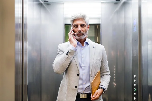 成熟的商人，与智能手机在电梯里. — 图库照片