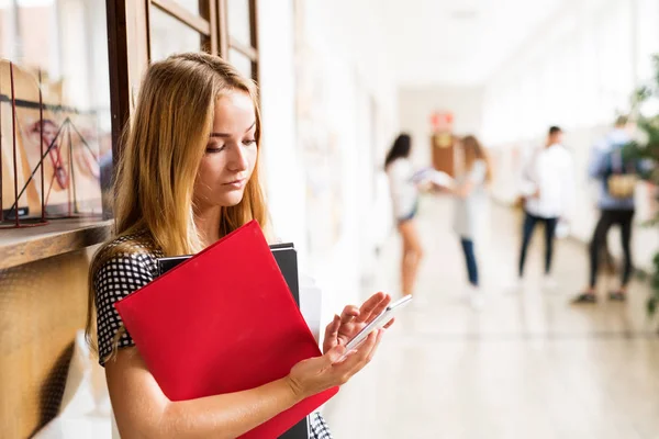 Tienermeisje met smartphone in high school hal tijdens pauze. — Stockfoto