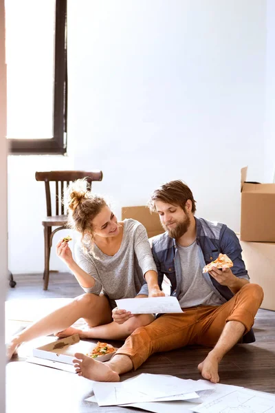 Young couple moving in new house, eating pizza. — Stock Photo, Image