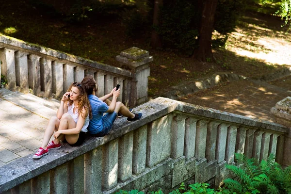 Jong (echt) paar met smartphones in de stad zit op betonnen muur. — Stockfoto