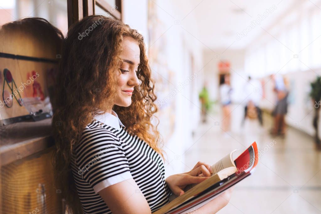 Teenage girl with notebooks in high school hall during break.