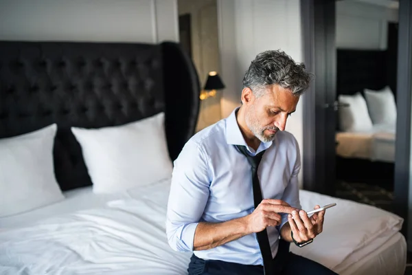 Mogen affärsman med smartphone i ett hotellrum. — Stockfoto