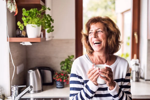 Mujer mayor sosteniendo una taza de café en la cocina . — Foto de Stock