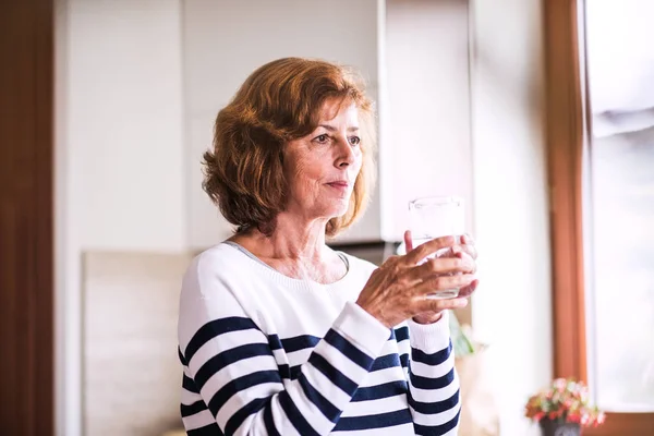 Mujer mayor sosteniendo un vaso de agua en la cocina . — Foto de Stock