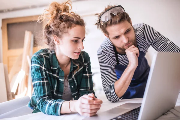 Pareja joven con portátil en el taller de carpintero . — Foto de Stock