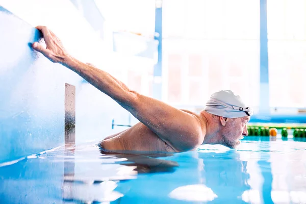 Senior man in een overdekt zwembad. — Stockfoto