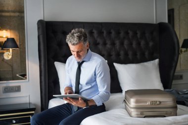 Bir otel odasında tablet ile olgun iş adamı.