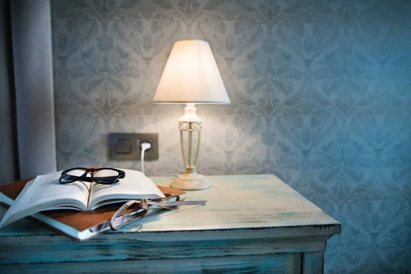 A lamp and a book on a bedside table in a hotel room.