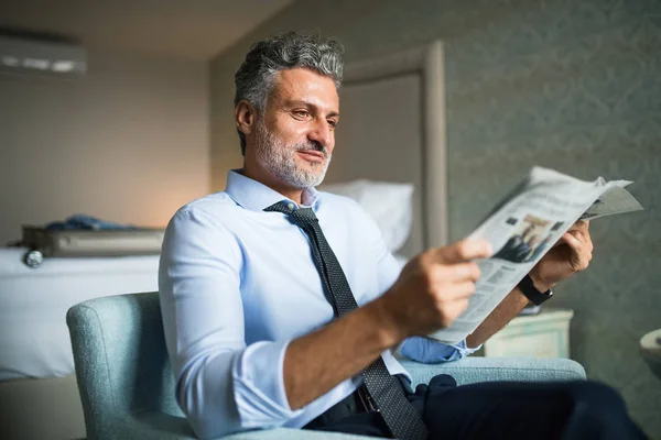 Mature businessman reading newspapers in a hotel room. — Stock Photo, Image