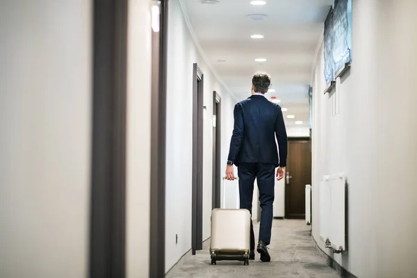 Homem de negócios maduro andando com bagagem em um corredor do hotel . — Fotografia de Stock