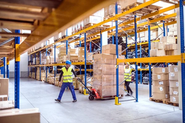 Magazijn werknemers trekken een pallettruck. — Stockfoto