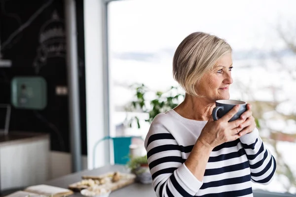 Senior vrouw met een kopje koffie in de keuken. — Stockfoto