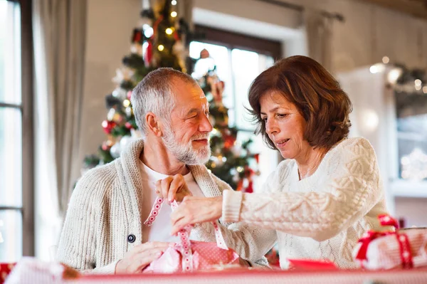 Casal sênior em camisolas embrulhando presentes de Natal juntos . — Fotografia de Stock