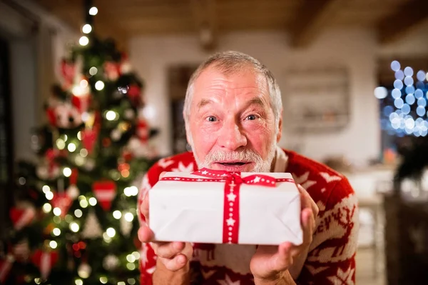 Senior man in front of Christmas tree holding a gift.