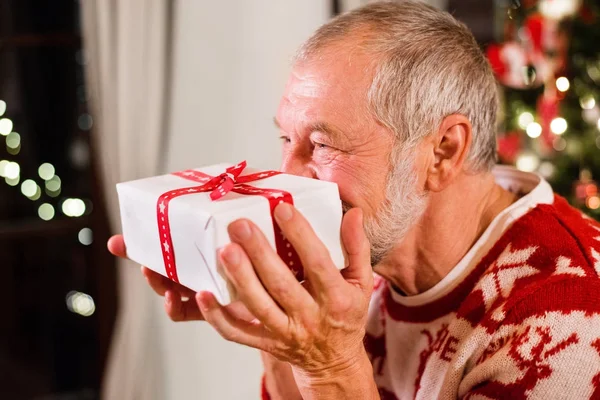 Senior mannen framför julgranen innehar en gåva. — Stockfoto