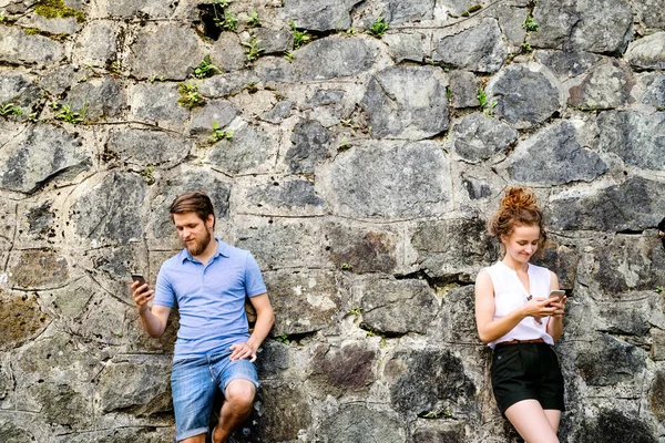Mladý pár s chytrými telefony proti kamenné zdi ve městě. — Stock fotografie
