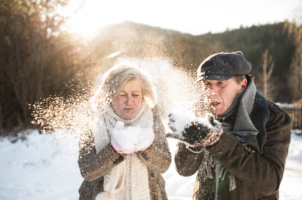 Beautiful senior couple blowing snow in sunny winter nature — Stock Photo, Image