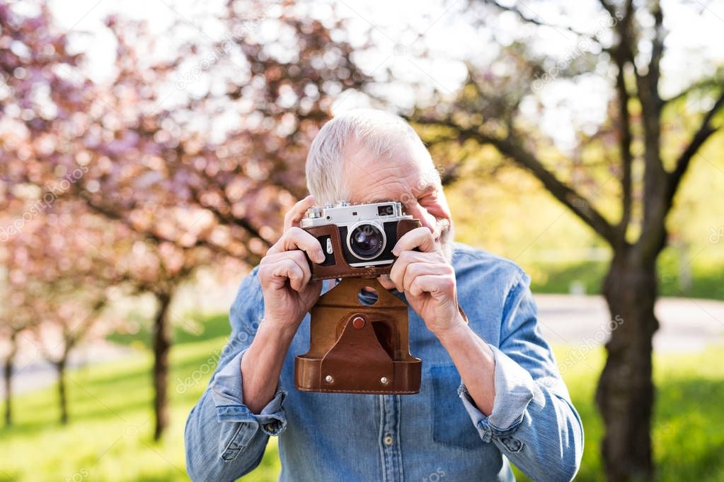 Senior man outside in spring nature taking pictures.