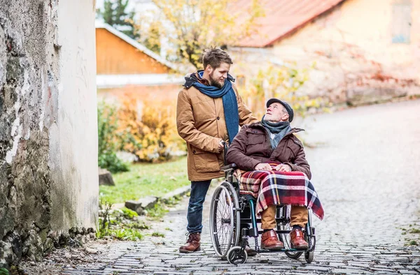 Senior father in wheelchair and young son on a walk. — Stock Photo, Image
