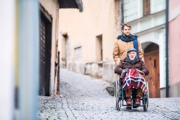 Padre mayor en silla de ruedas e hijo pequeño en un paseo . — Foto de Stock