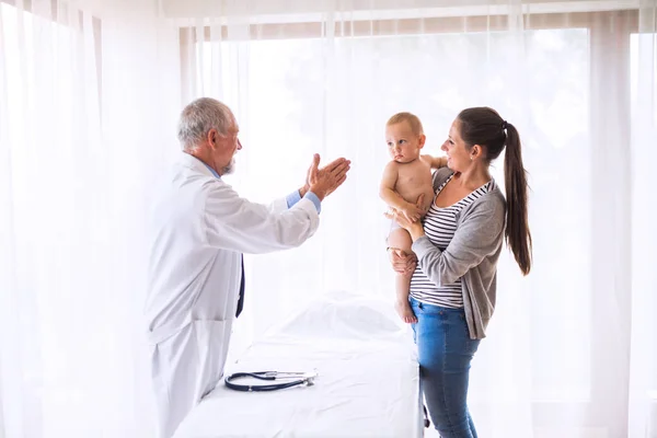 Médico senior, madre y un bebé en un consultorio . — Foto de Stock