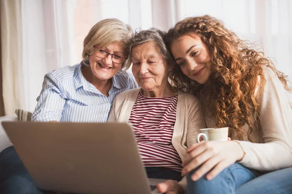 Een tienermeisje, moeder en grootmoeder met laptop thuis. — Stockfoto