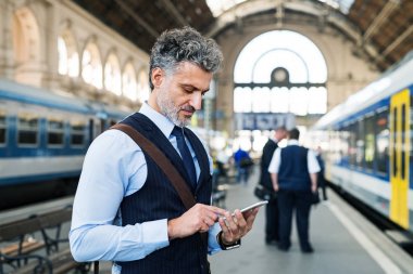Olgun işadamı ile smartphone bir tren istasyonu.