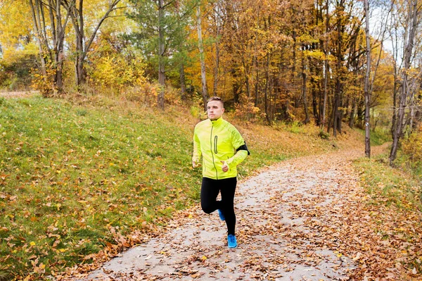 Junge Sportlerin mit Smartphone läuft im Herbst im Park. — Stockfoto