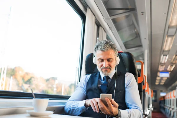 Mature businessman with smartphone travelling by train. — Stock Photo, Image