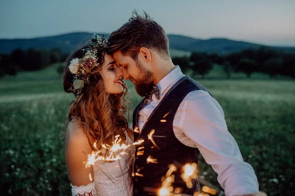 Mooie bruid en bruidegom met wonderkaarsen op een weide. — Stockfoto