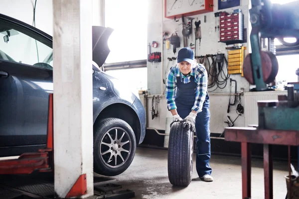 Mecânico feminino sênior reparando um carro em uma garagem . — Fotografia de Stock