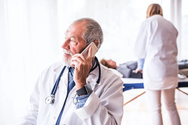 Médico senior con smartphone en su consultorio . —  Fotos de Stock