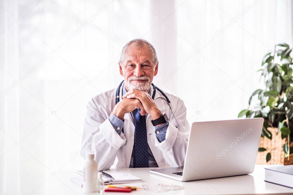 Senior doctor with laptop sitting at the office desk.