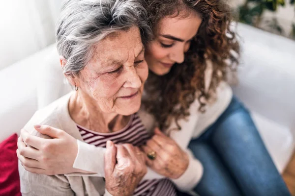 Een tienermeisje met grootmoeder thuis, knuffelen. — Stockfoto
