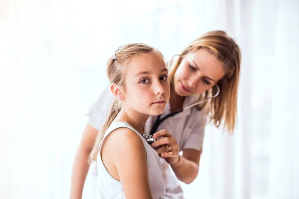 Doctora joven examinando a una niña pequeña en su consultorio . —  Fotos de Stock