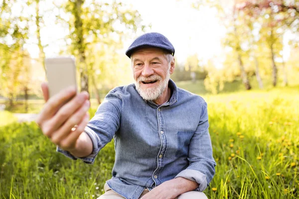 Starší muž s smartphone mimo v jarní přírodě. — Stock fotografie