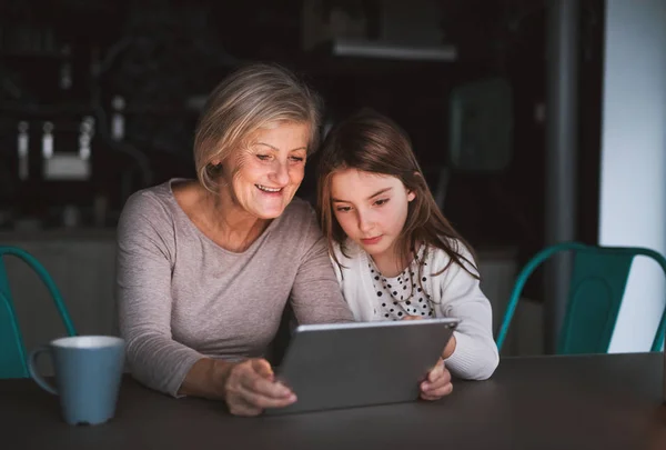 Een klein meisje en grootmoeder met Tablet PC thuis. — Stockfoto