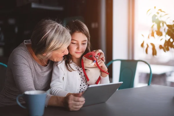 Een klein meisje en grootmoeder met Tablet PC thuis. — Stockfoto