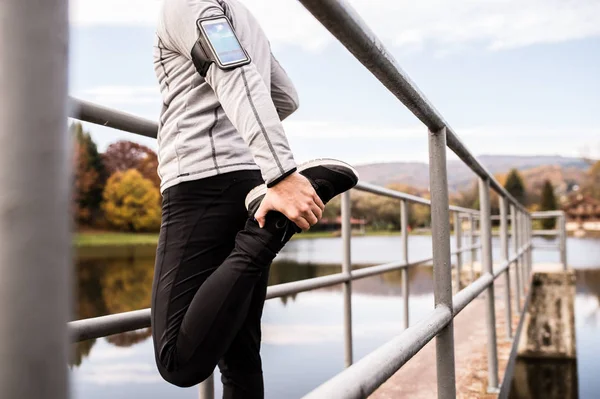 Junge Sportlerin streckt sich mit Smartphone im Park. — Stockfoto